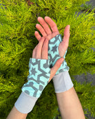 Two hands wearing organic cotton wrist warmers, mint fabric with geometric print.