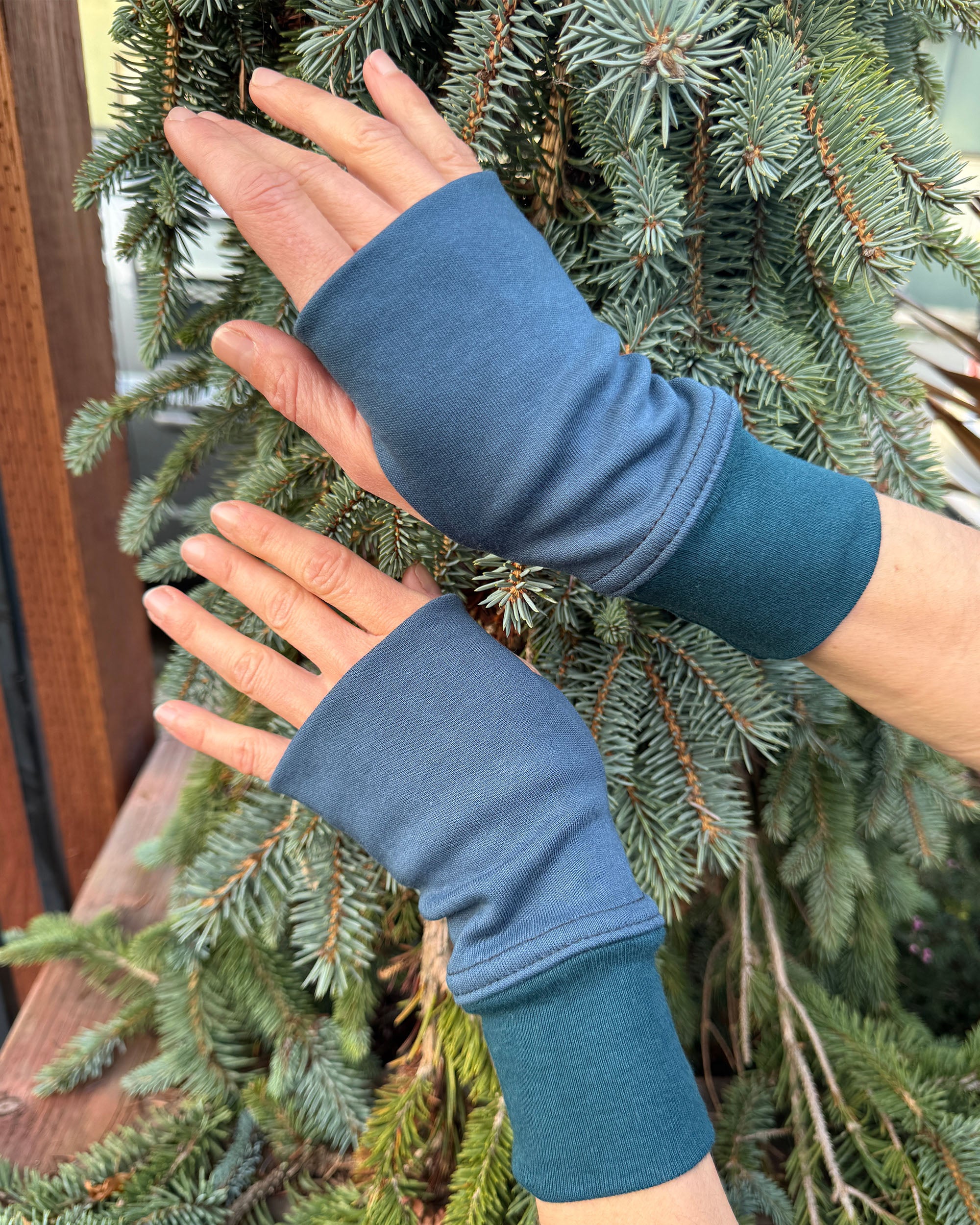 Hands wearing dark blue organic cotton hand warmers shown with natural background.