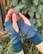 Female hands wearing dark blue organic cotton hand warmers shown with leafy background.
