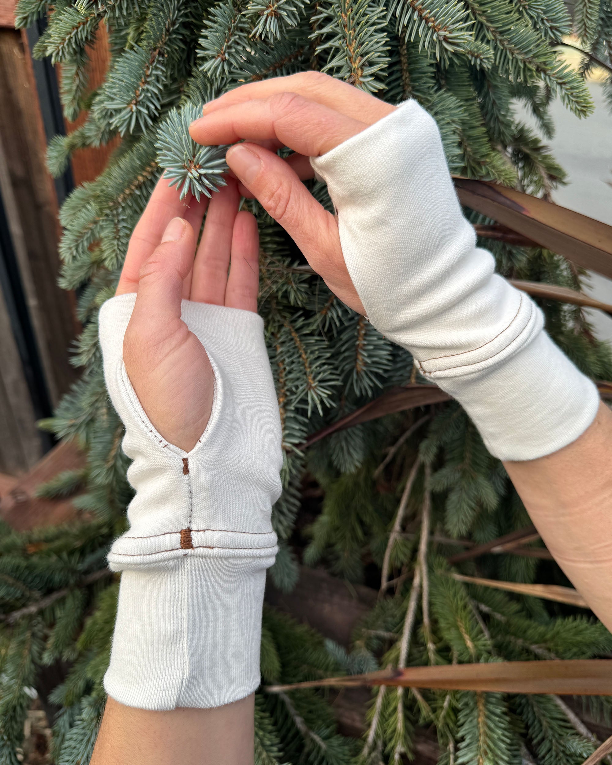 Female hands wearing organic cotton hand warmers, un-dyed fabric with spruce tree.