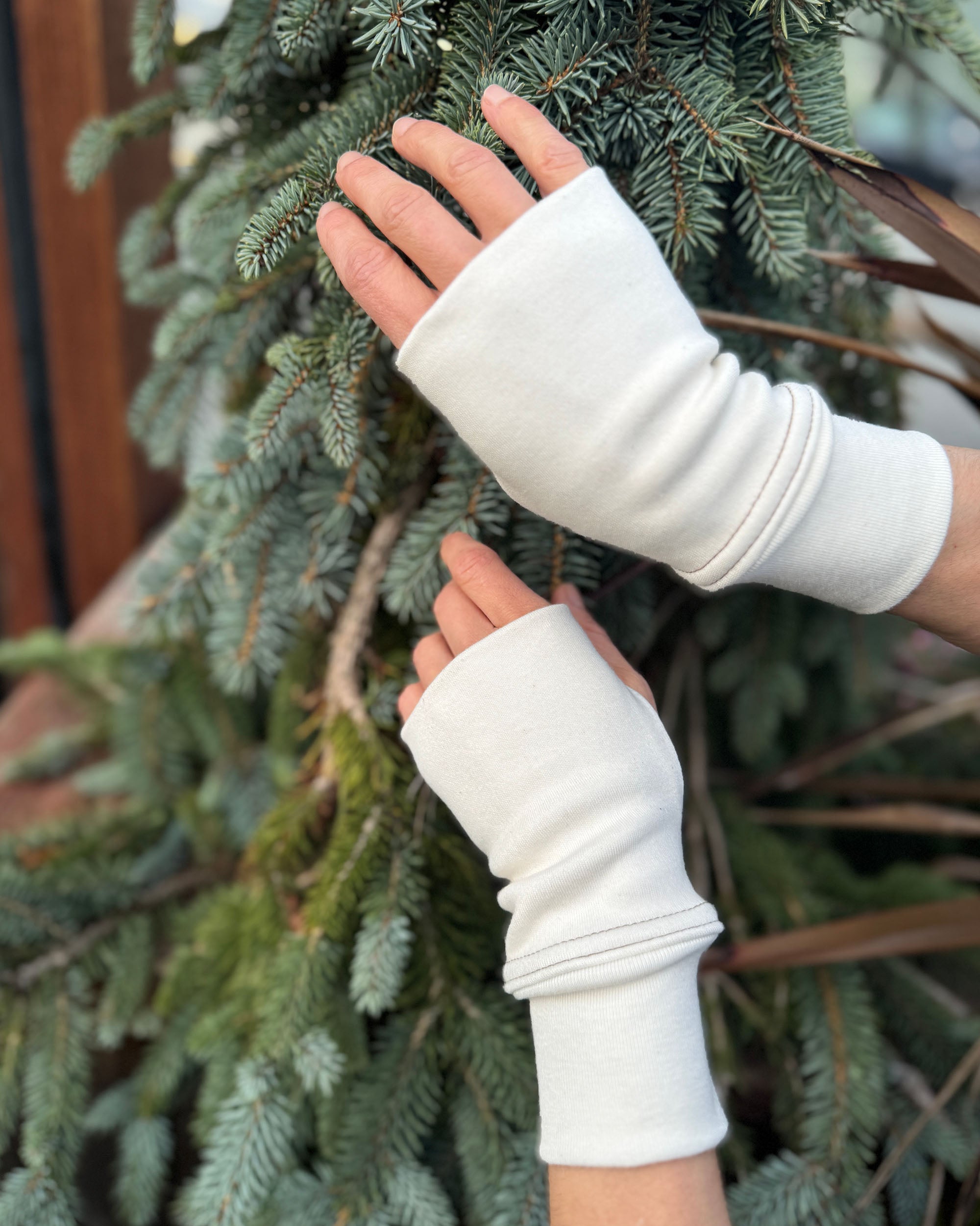 Two hands wearing organic cotton wrist warmers, un-dyed fabric with natural background.