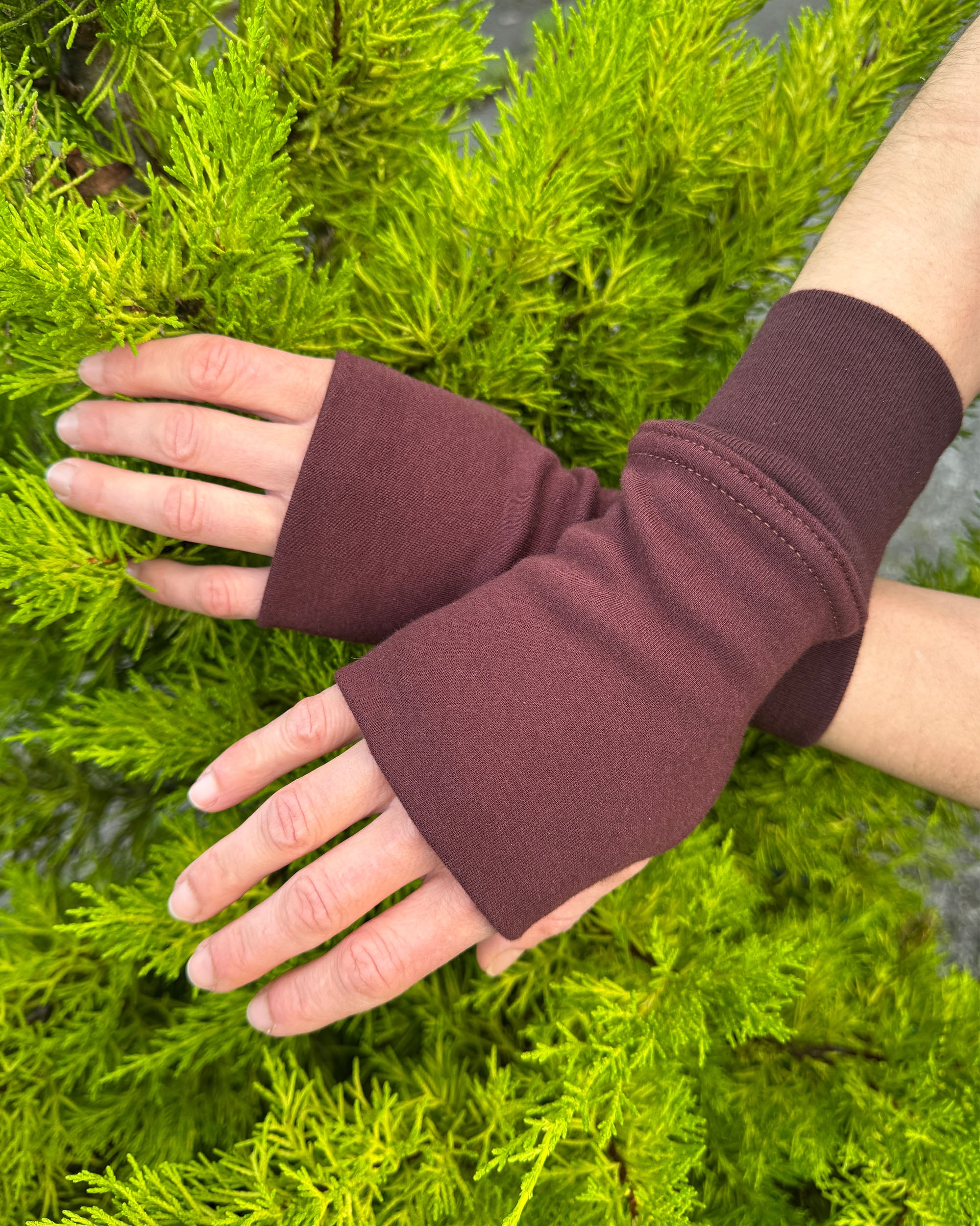 Female hands wearing organic cotton hand warmers, brown solid fabric with natural background.