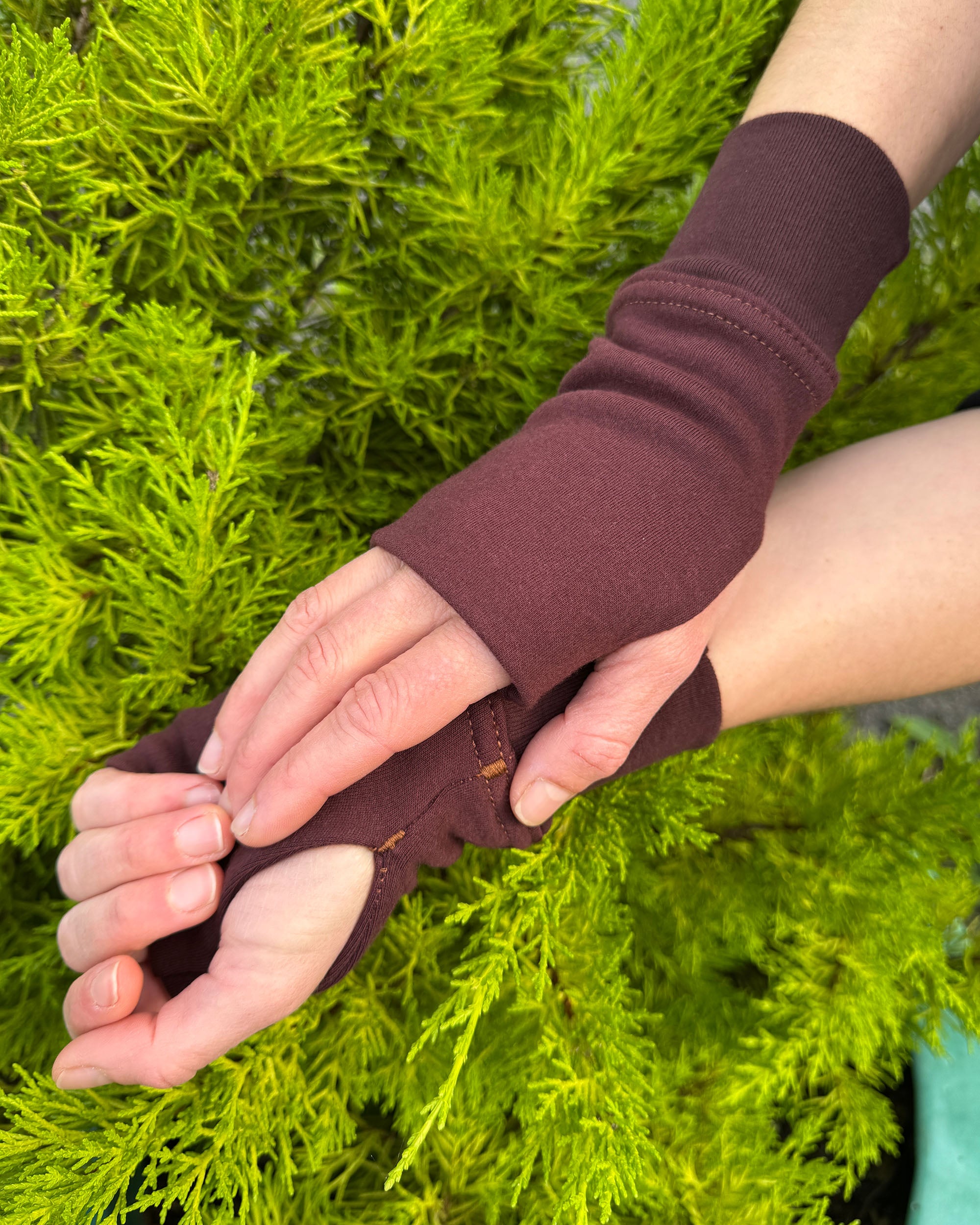 Two hands wearing organic cotton wrist warmers, brown colored fabric with natural background.