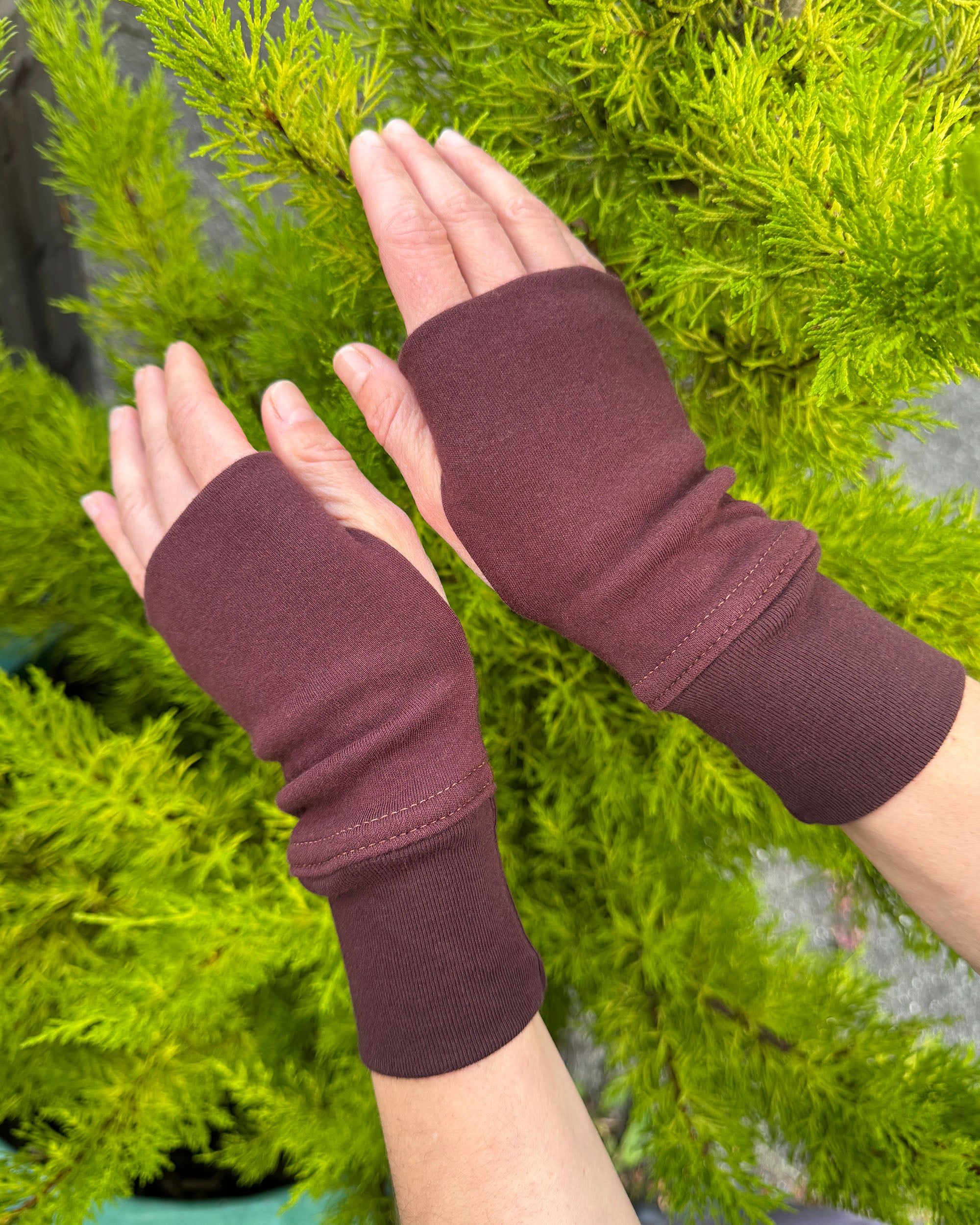 Female hands wearing organic cotton hand warmers, brown fabric with natural background.