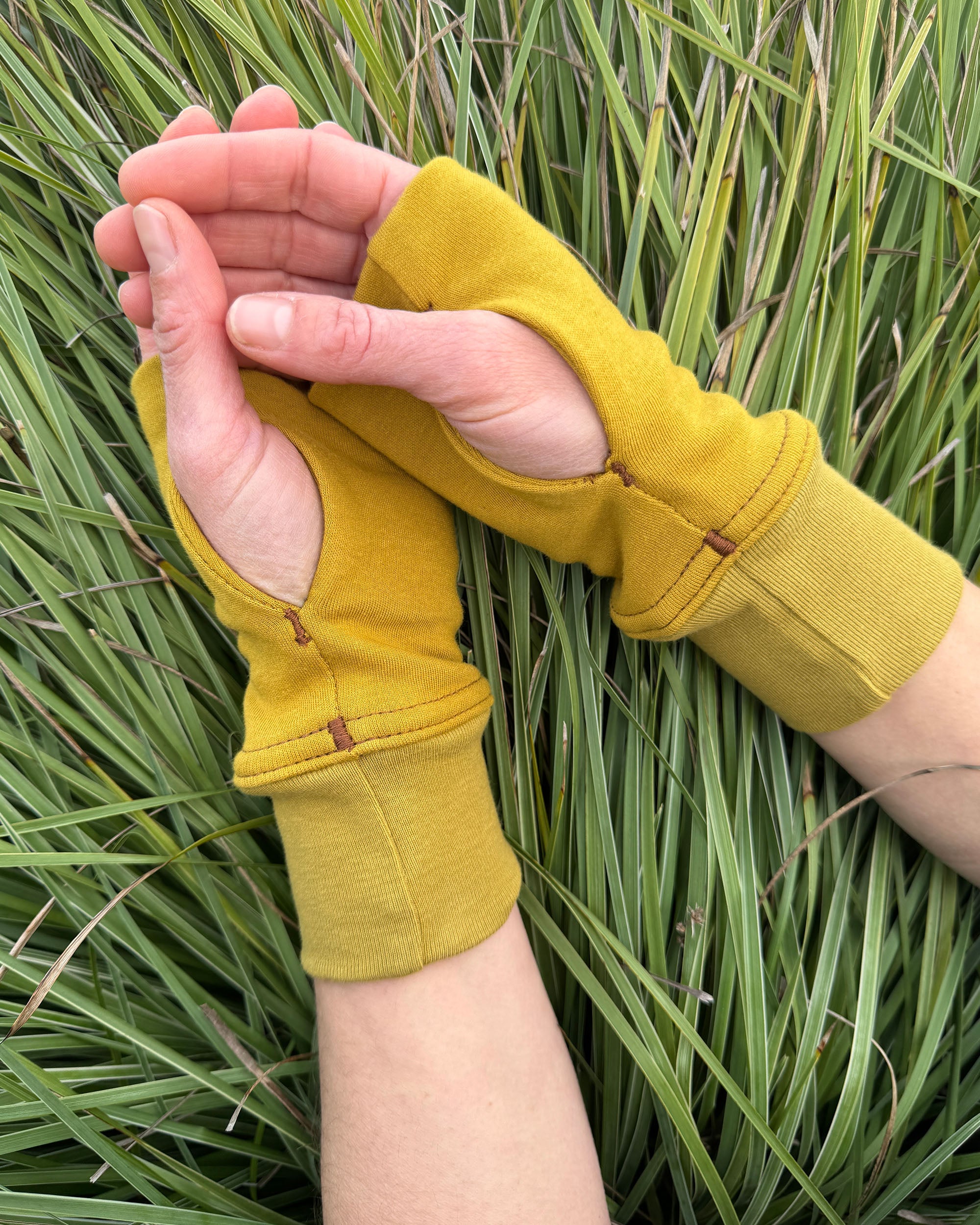 Female hands wearing organic cotton hand warmers, with a natural background.