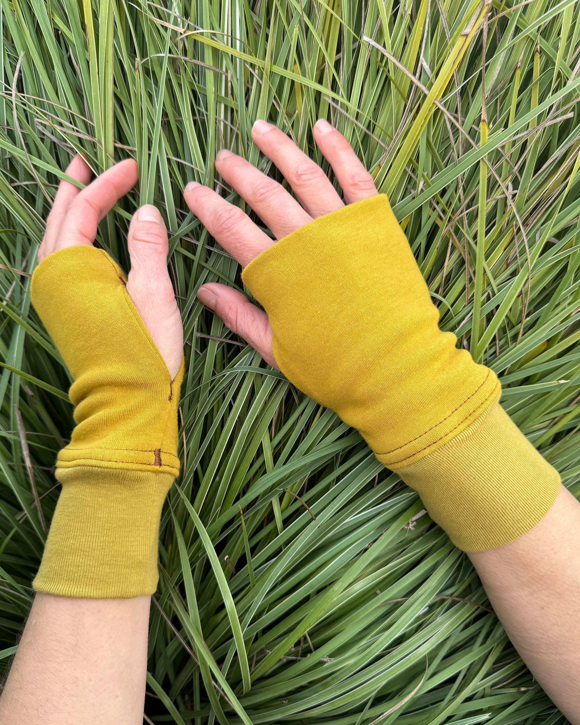 Female hands wearing organic cotton hand warmers, yellow solid fabric with natural background.
