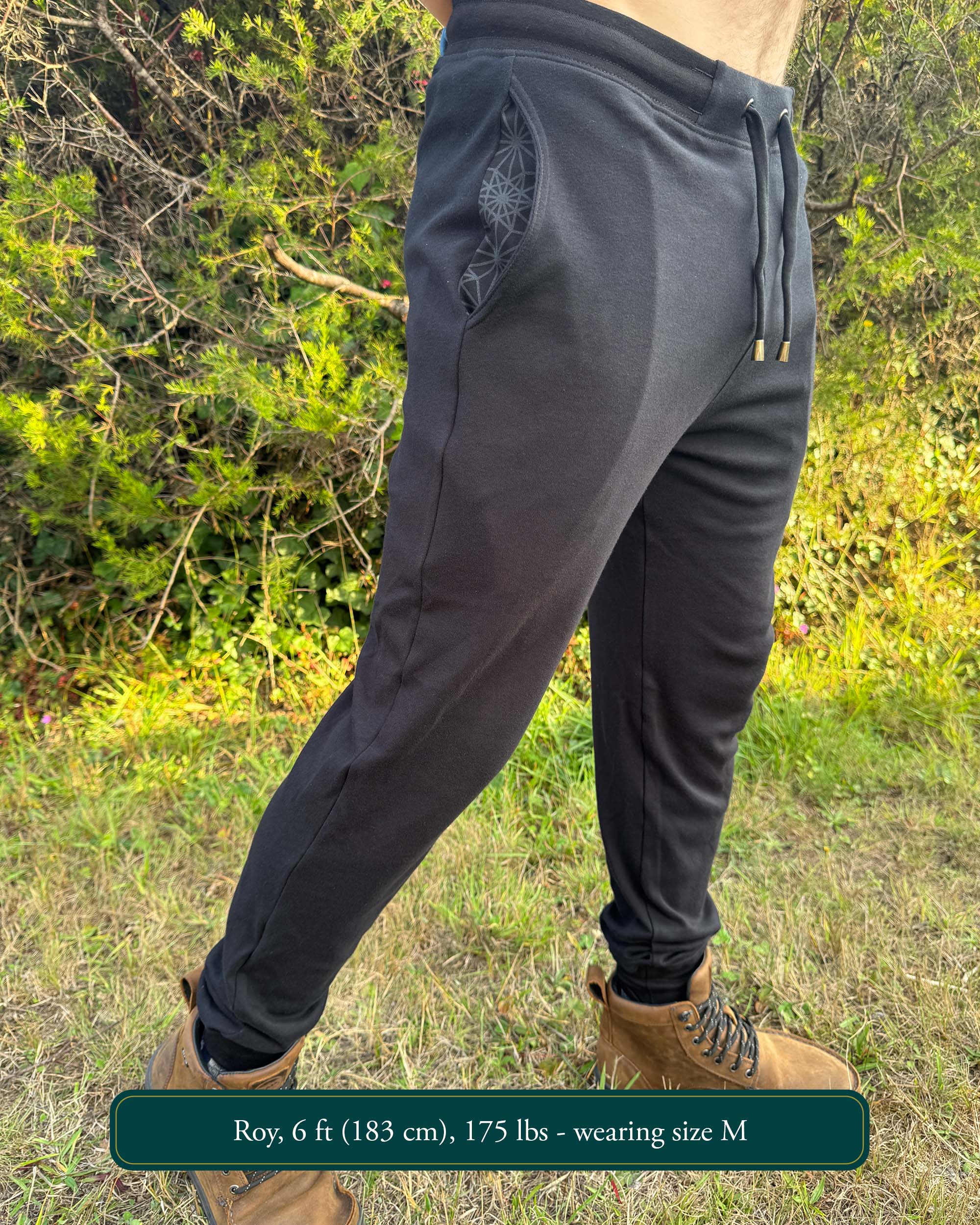 Organic cotton joggers, black fabric, right side full body view on male model in nature.