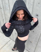 Fitted crop hoodie with cowl hood, black fabric with geometric print, front view.