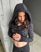 Fitted crop hoodie with cowl hood, black fabric with geometric print, top view on female model.