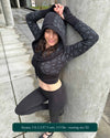 Fitted crop hoodie with cowl hood, black fabric with geometric print, left side view on female model.