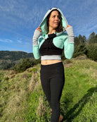 Fitted crop hoodie with cowl hood, mint fabric with black accent, front side view on model in nature.
