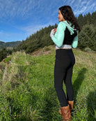 Fitted crop hoodie with cowl hood, mint fabric with black accent, back left side view on model in nature.