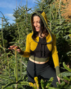 Fitted crop hoodie with cowl hood, yellow fabric with black accent, front side view on model in trees.