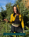Fitted crop hoodie with cowl hood, yellow fabric with black and green accents, worn by female model.