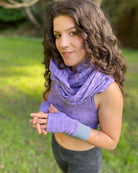 Female model wearing matching set of crop top, infinity scarf and fingerless gloves, purple organic cotton fabric with geometric print, front left view.