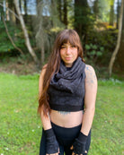 Female model wearing matching set of crop top, infinity scarf and fingerless gloves, black organic cotton fabric with geometric print, front view in nature.