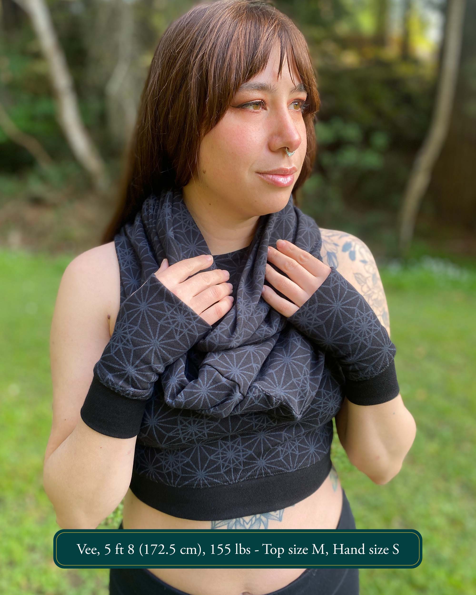 Female model wearing matching set of crop top, infinity scarf and fingerless gloves, black fabric with geometric print, front view.