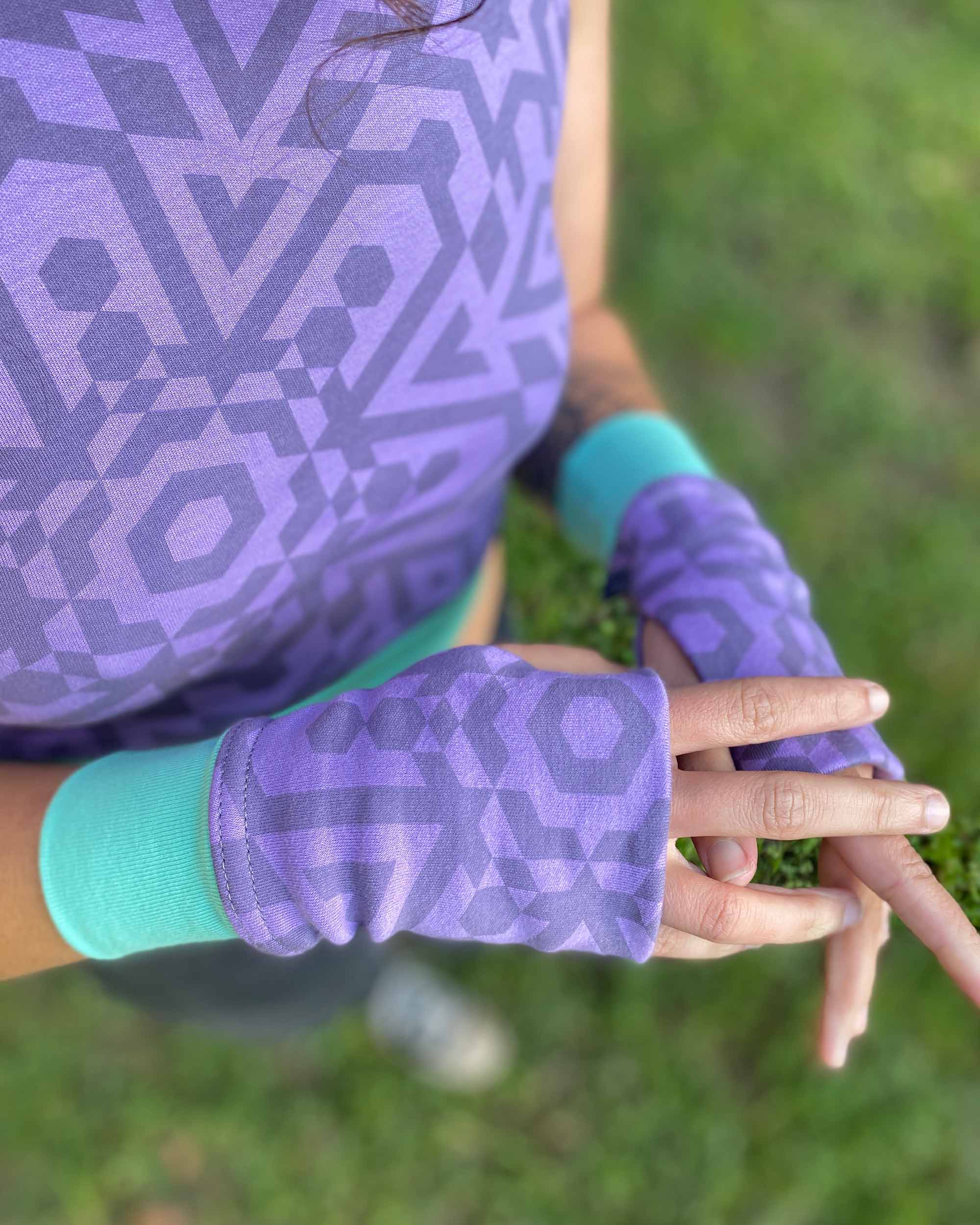 Female model wearing matching set of crop top, infinity scarf and fingerless gloves, lavender organic cotton fabric with geometric print, close up of gloves.