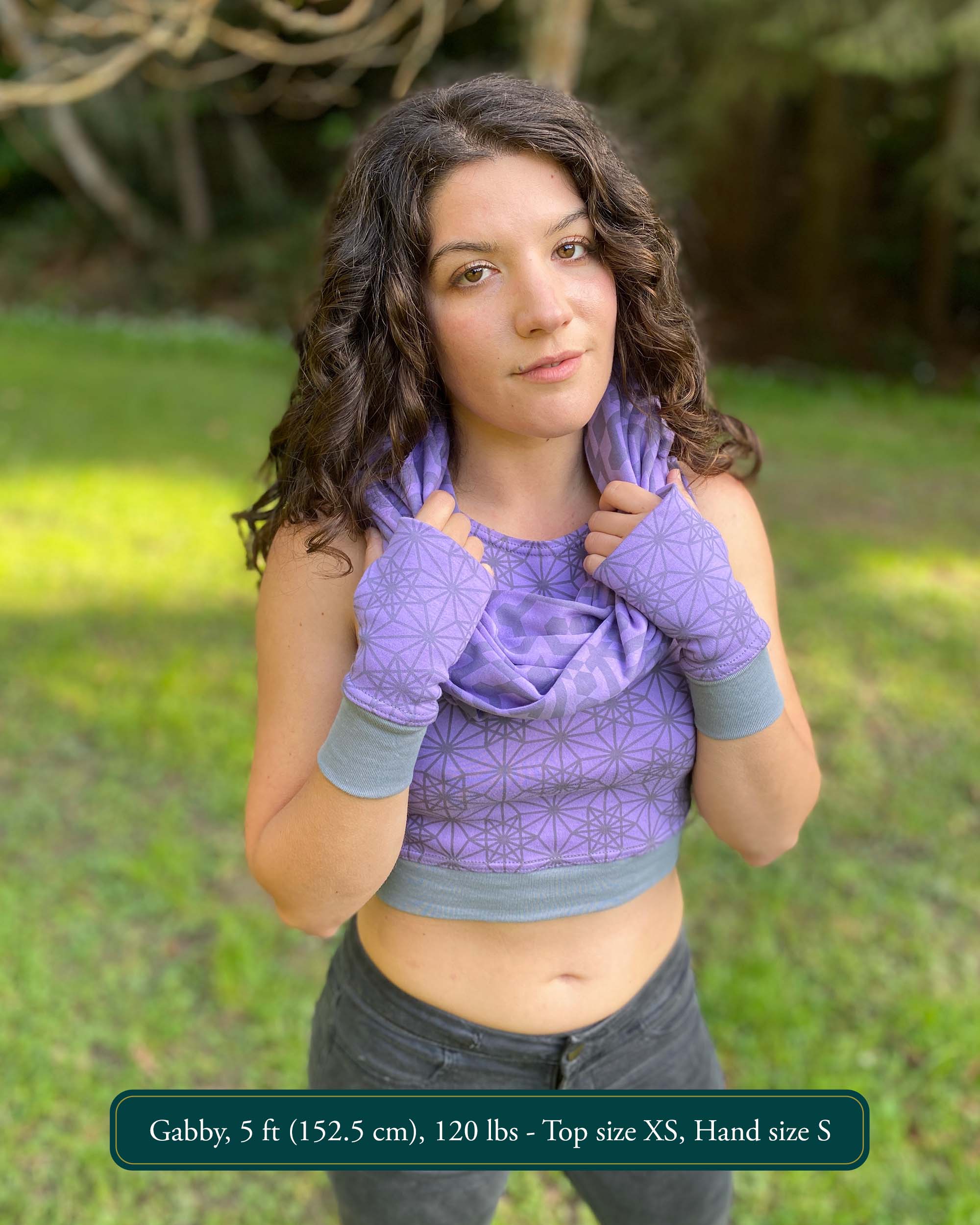 Female model wearing matching set of crop top, infinity scarf and fingerless gloves, purple organic cotton fabric with geometric print, front view.