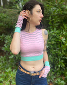 Female model wearing matching set of crop top and fingerless gloves, pink organic cotton fabric with geometric stripes, front view.
