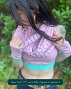 Female model wearing matching set of crop top, infinity scarf and fingerless gloves, pink organic cotton fabric with geometric stripes, front view.