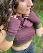 Female model wearing matching set of crop top, infinity scarf and fingerless gloves, brown organic cotton fabric with geometric print, close up view.