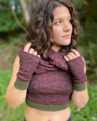 Female model wearing matching set of crop top, infinity scarf and fingerless gloves, brown organic cotton fabric with geometric print, front view.