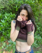 Female model wearing matching set of crop top, infinity scarf and fingerless gloves, brown organic cotton fabric with geometric print, front view in natural setting.