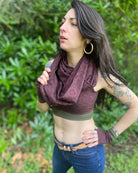 Female model wearing matching set of crop top, infinity scarf and fingerless gloves, brown organic cotton fabric with geometric print, front side view.