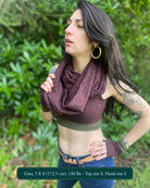 Female model wearing matching set of crop top, infinity scarf and fingerless gloves, brown organic cotton fabric with geometric print, left side view in nature.