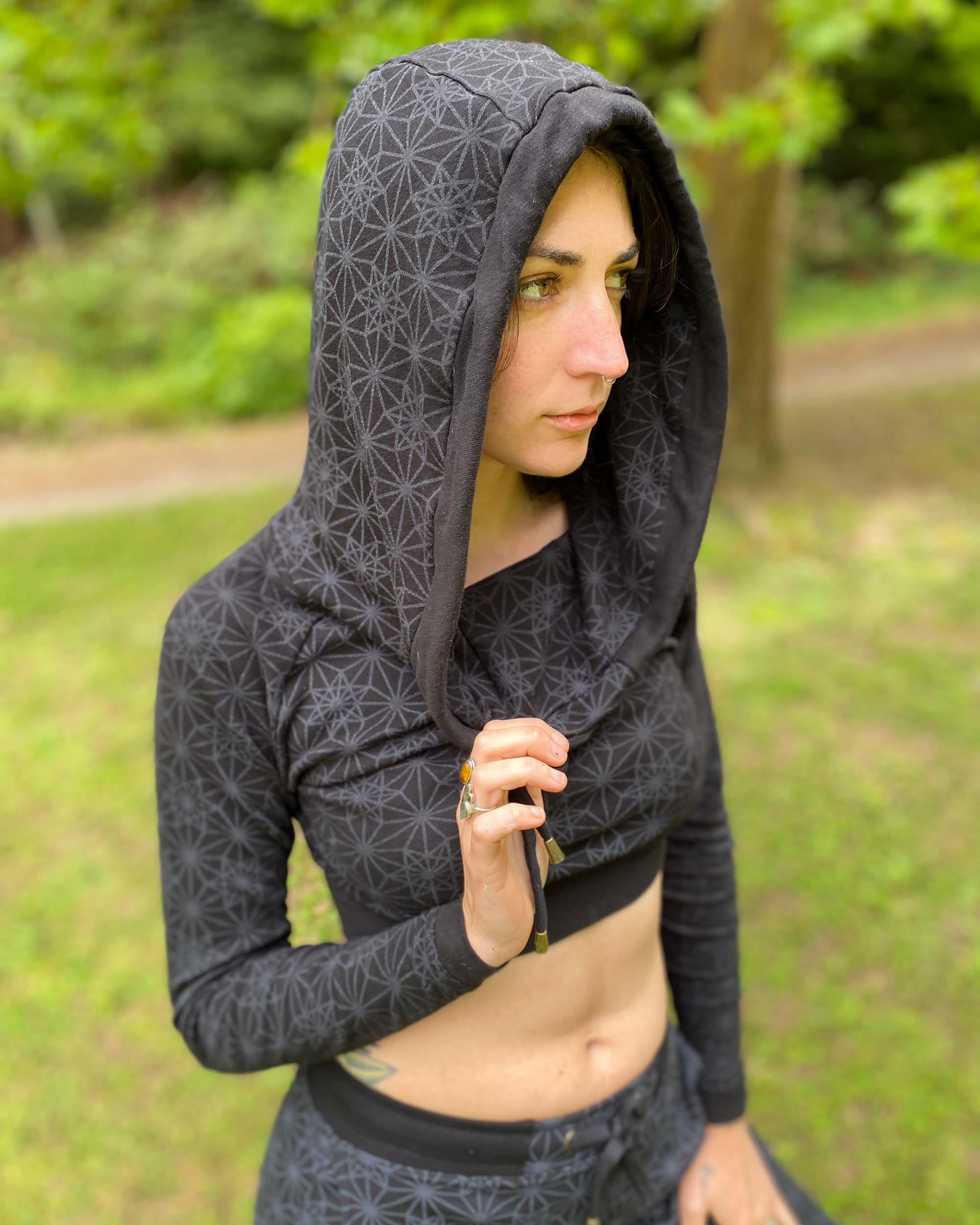 Women's matching two piece set, joggers and crop hoodie, black fabric with geometric print, worn with hood on.