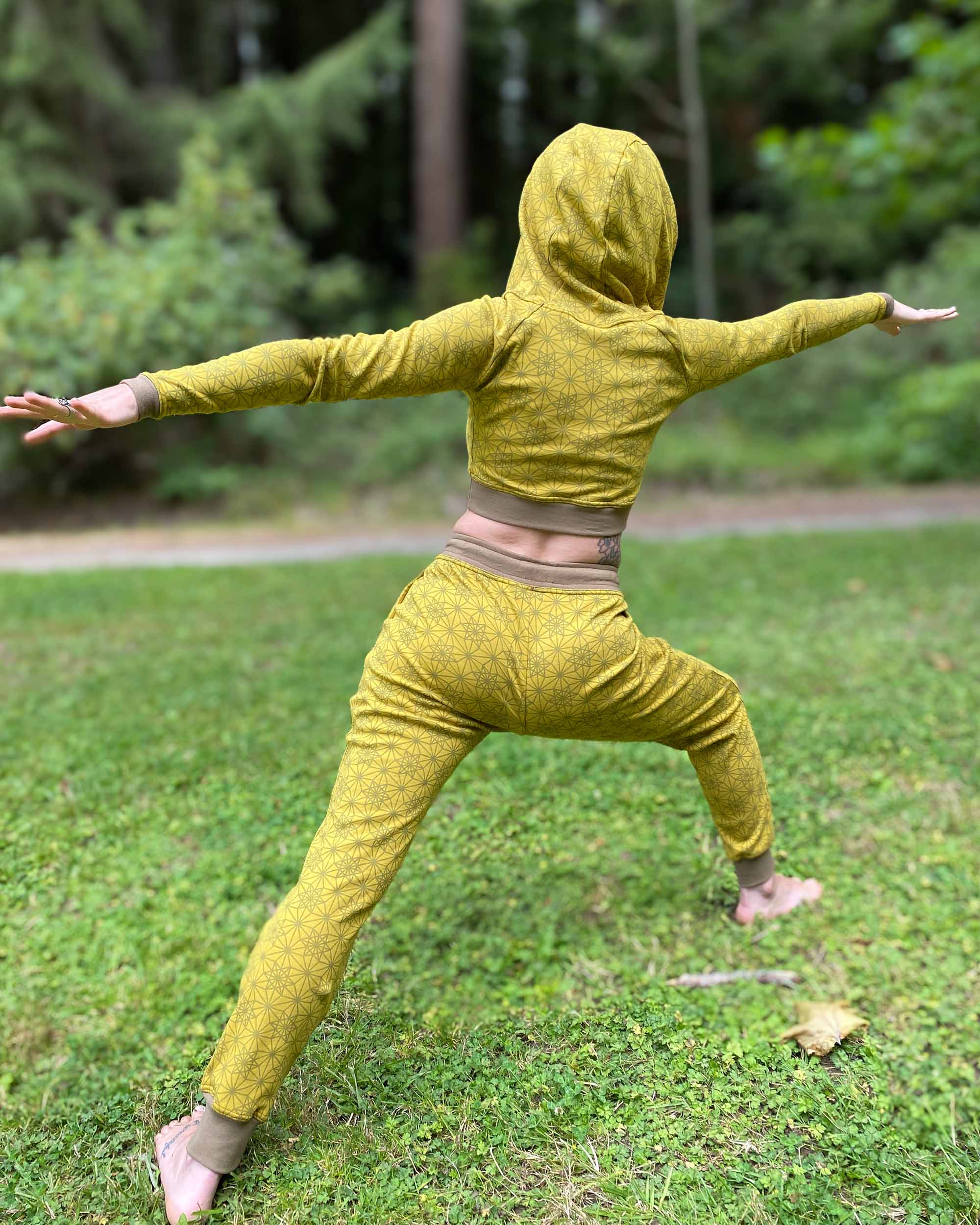 Women's matching two piece outfit, joggers and crop hoodie, yellow fabric with geometric print, model in yoga pose.