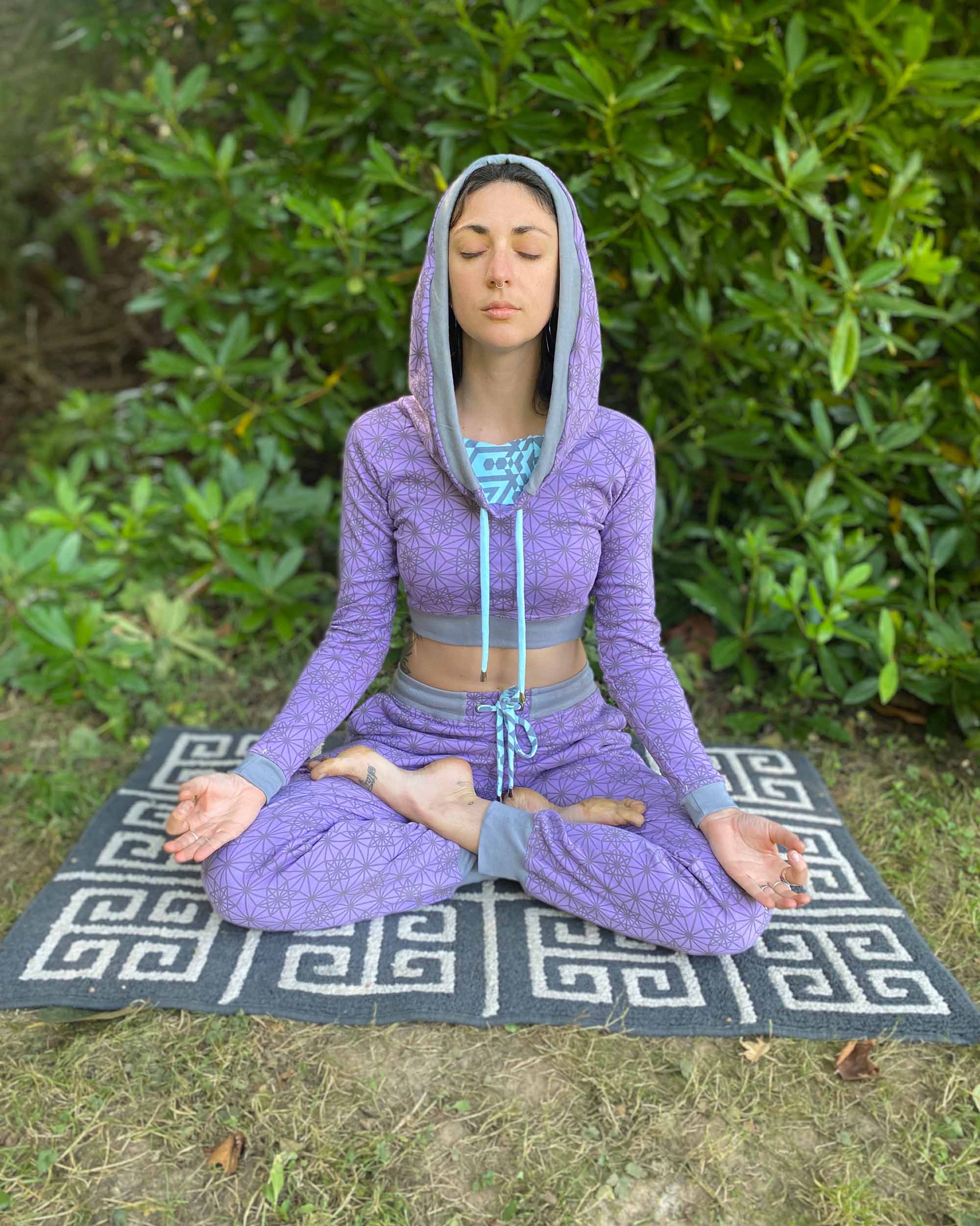 Matching two piece set, joggers and crop hoodie, lavender with geometric printed fabric, worn on female model in yoga pose.