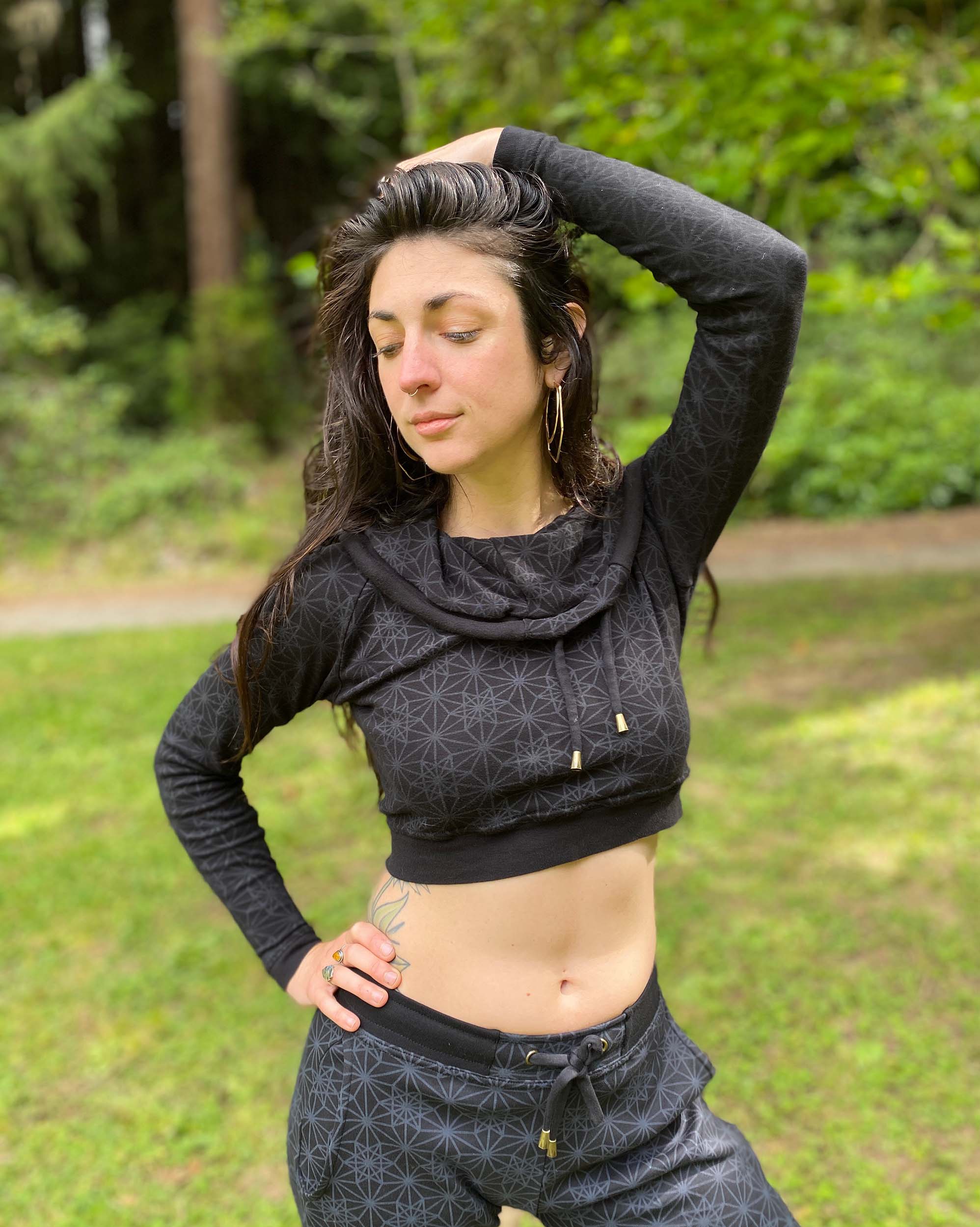 A woman wearing an organic cotton black crop hoodie with geometric print, with matching joggers, side view in a outdoor setting.