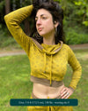 A woman wearing an organic cotton crop hoodie, yellow with geometric print, cowl neck and long sleeves, front view in a outdoor setting.