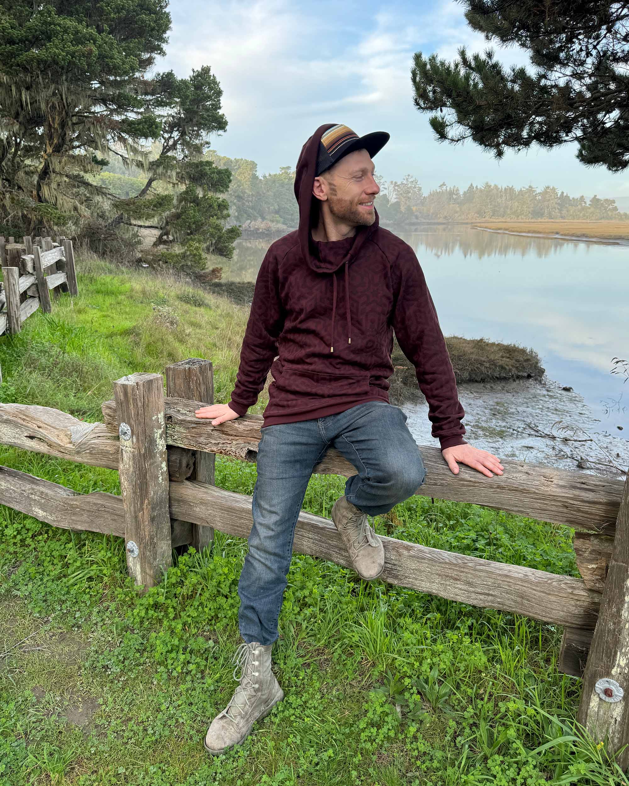 Organic cotton fleece unisex hoodie, reddish brown fabric with geometric print, front view, male model sitting.