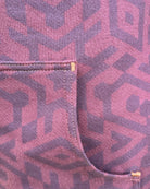 Organic cotton fleece unisex hoodie, reddish brown fabric with geometric print, close up view of pocket.