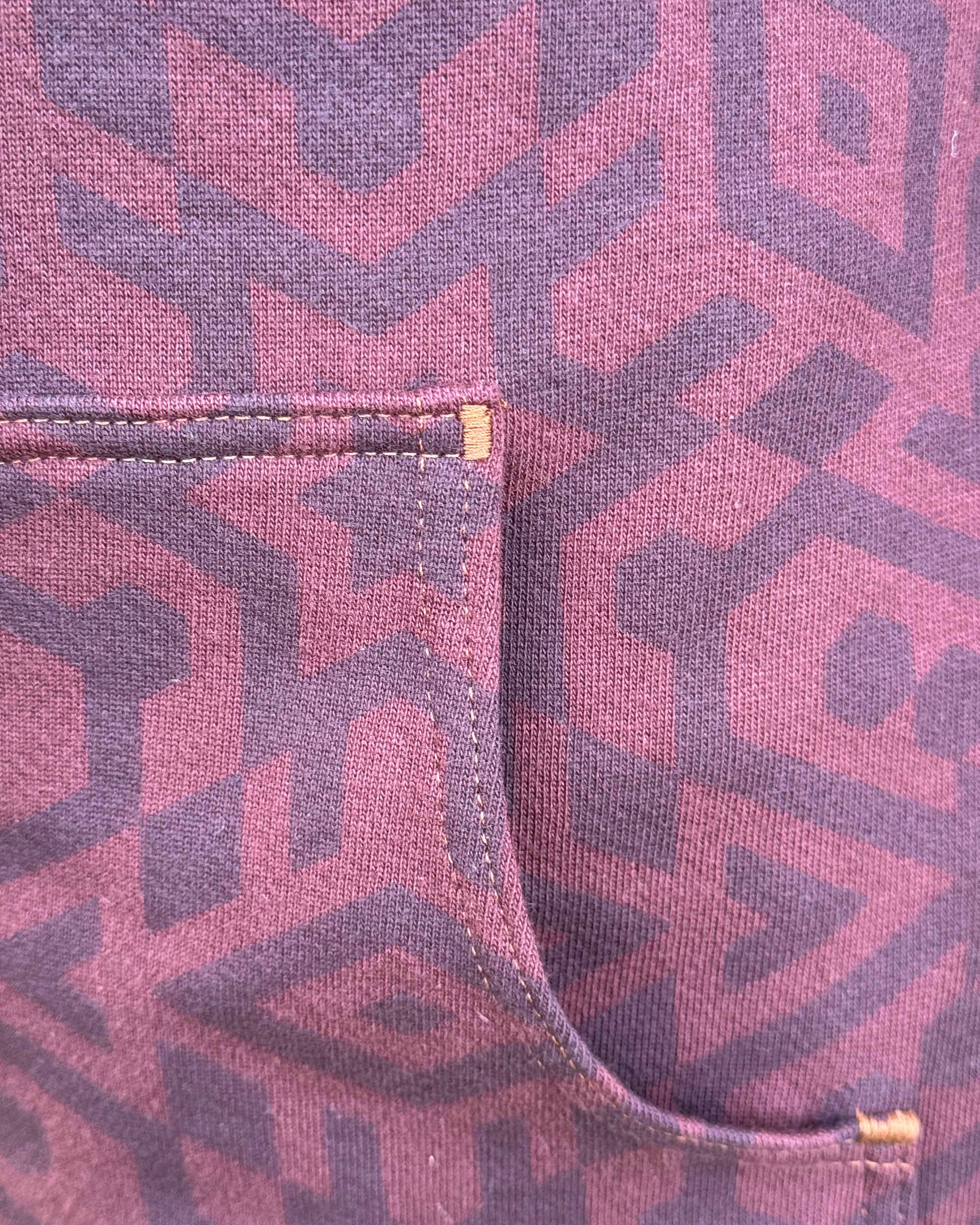 Organic cotton fleece unisex hoodie, reddish brown fabric with geometric print, close up view of pocket.