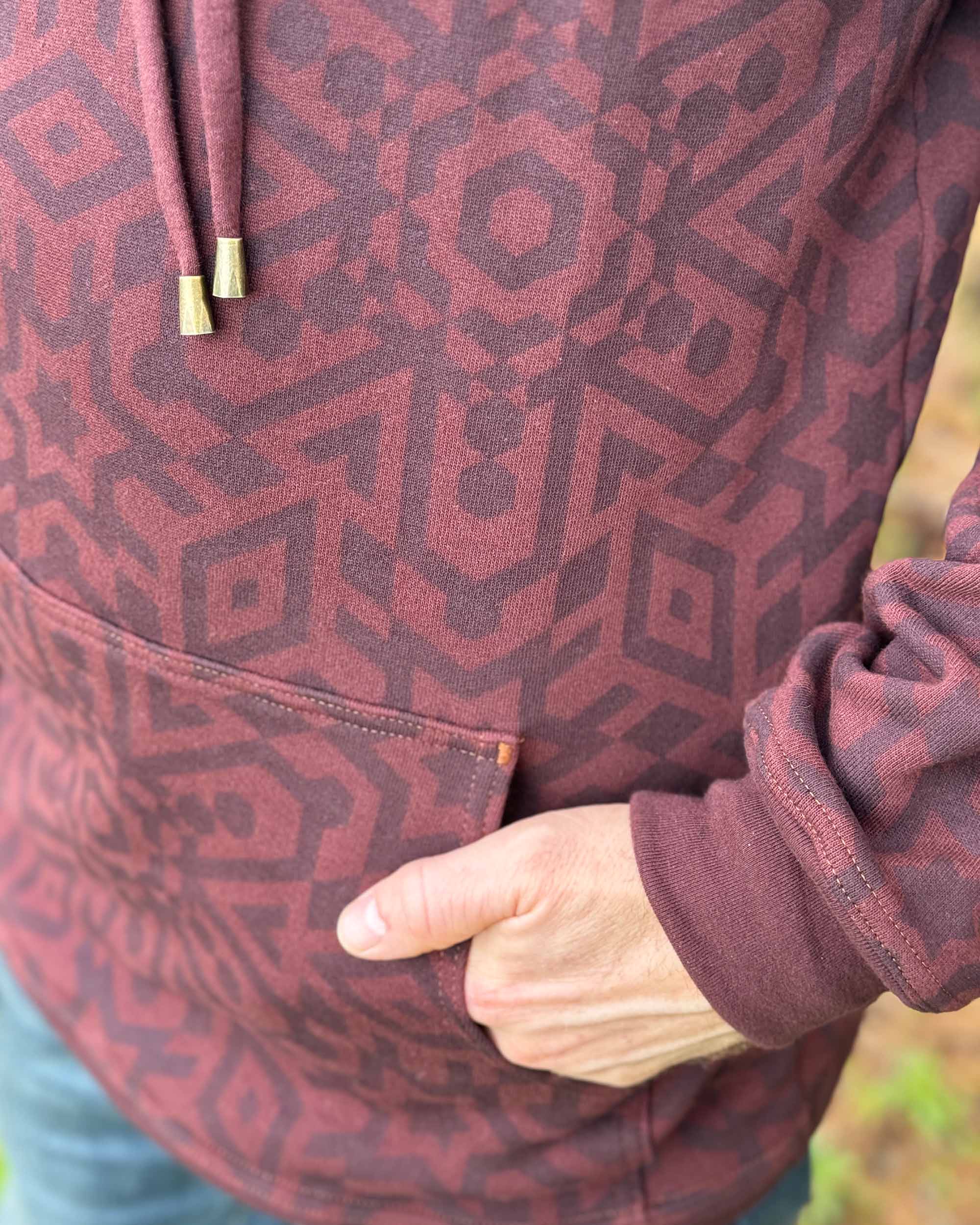 Organic cotton fleece unisex hoodie, reddish brown fabric with geometric print, close up view of front pocket.