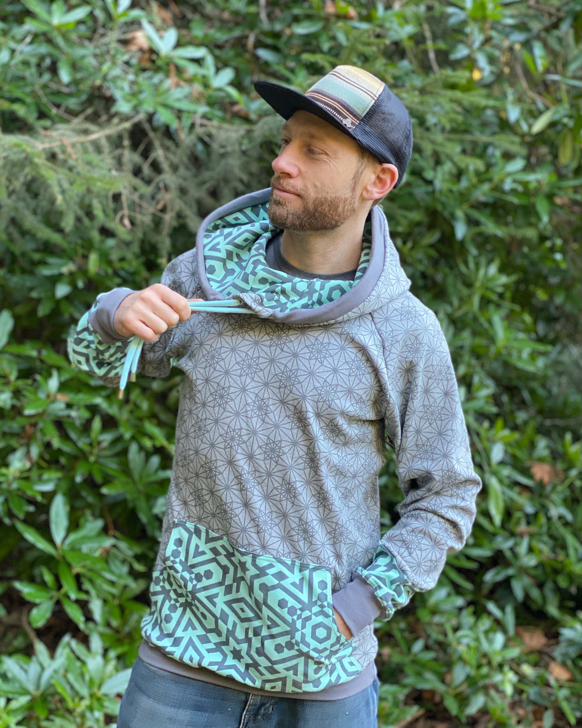 Organic cotton extra long unisex hoodie, grey fabric with geometric print, left side view of male model.