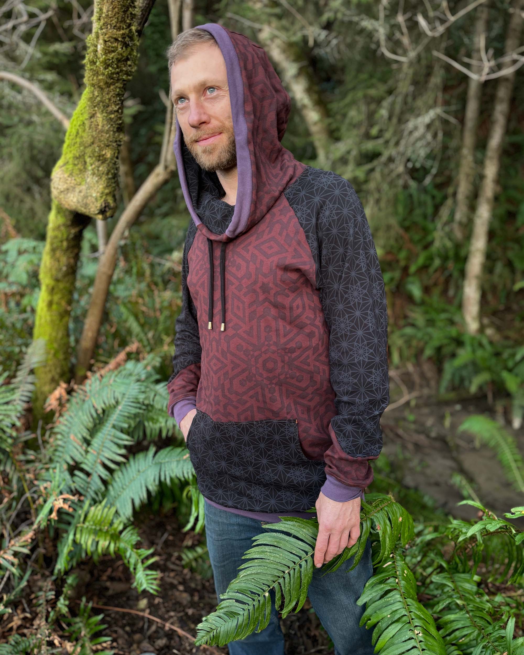 Extra long unisex hoodie, brown fabric with geometric print, right side view of male model in nature.