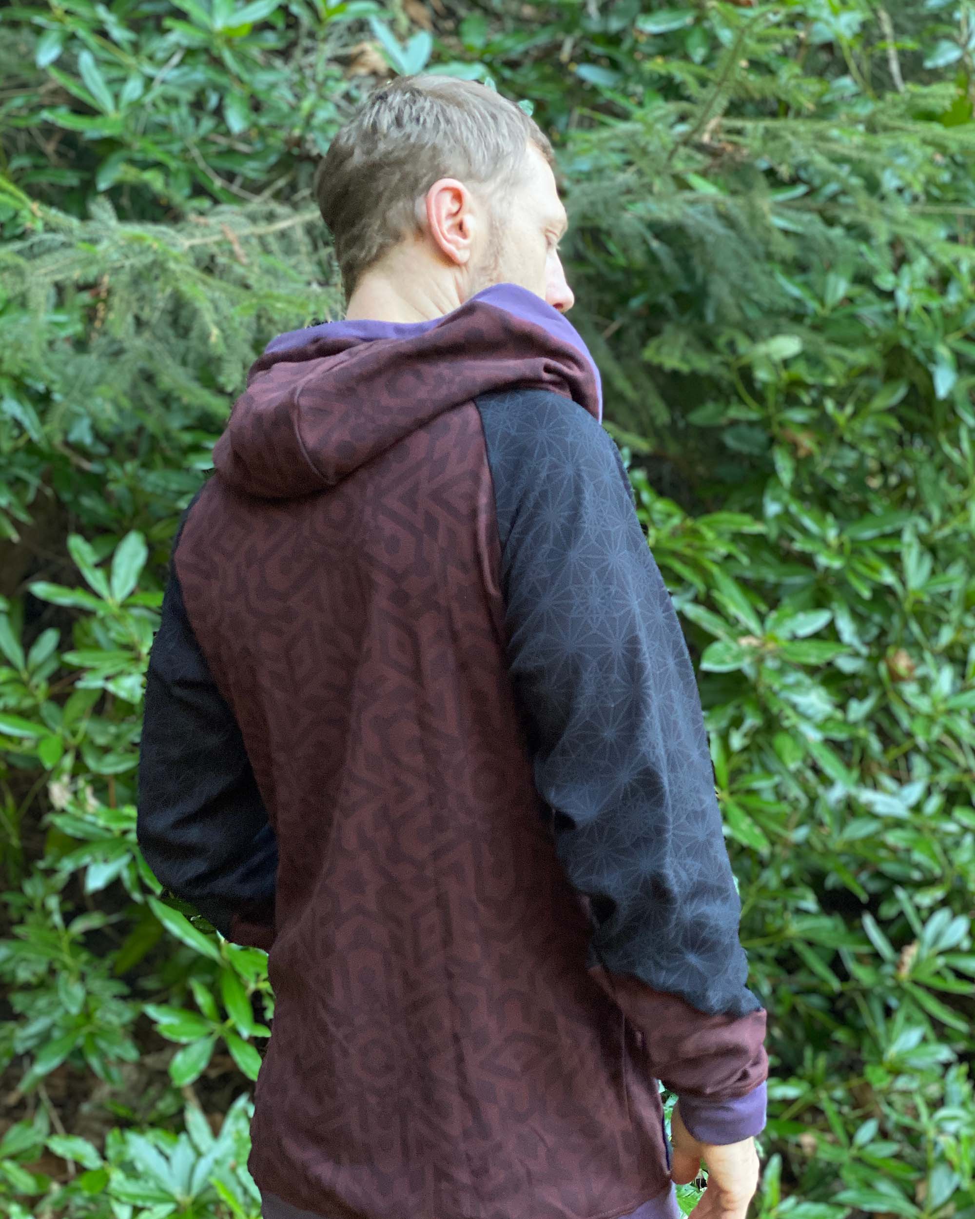 Organic cotton hoodie, reddish brown fabric with sacred geometry print, back view of male model.