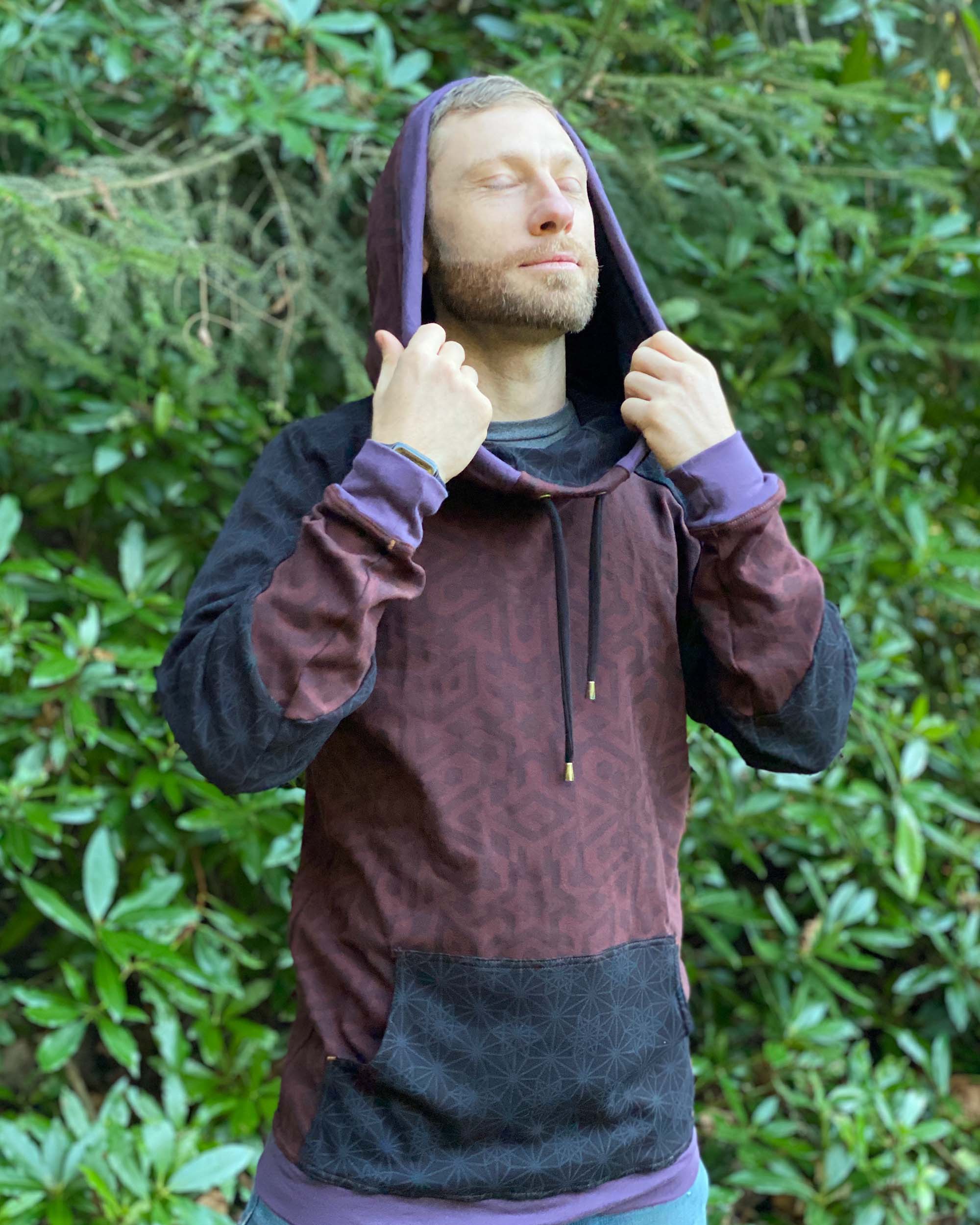 Organic cotton hoodie, reddish brown fabric with sacred geometry print, front view of male model in nature.