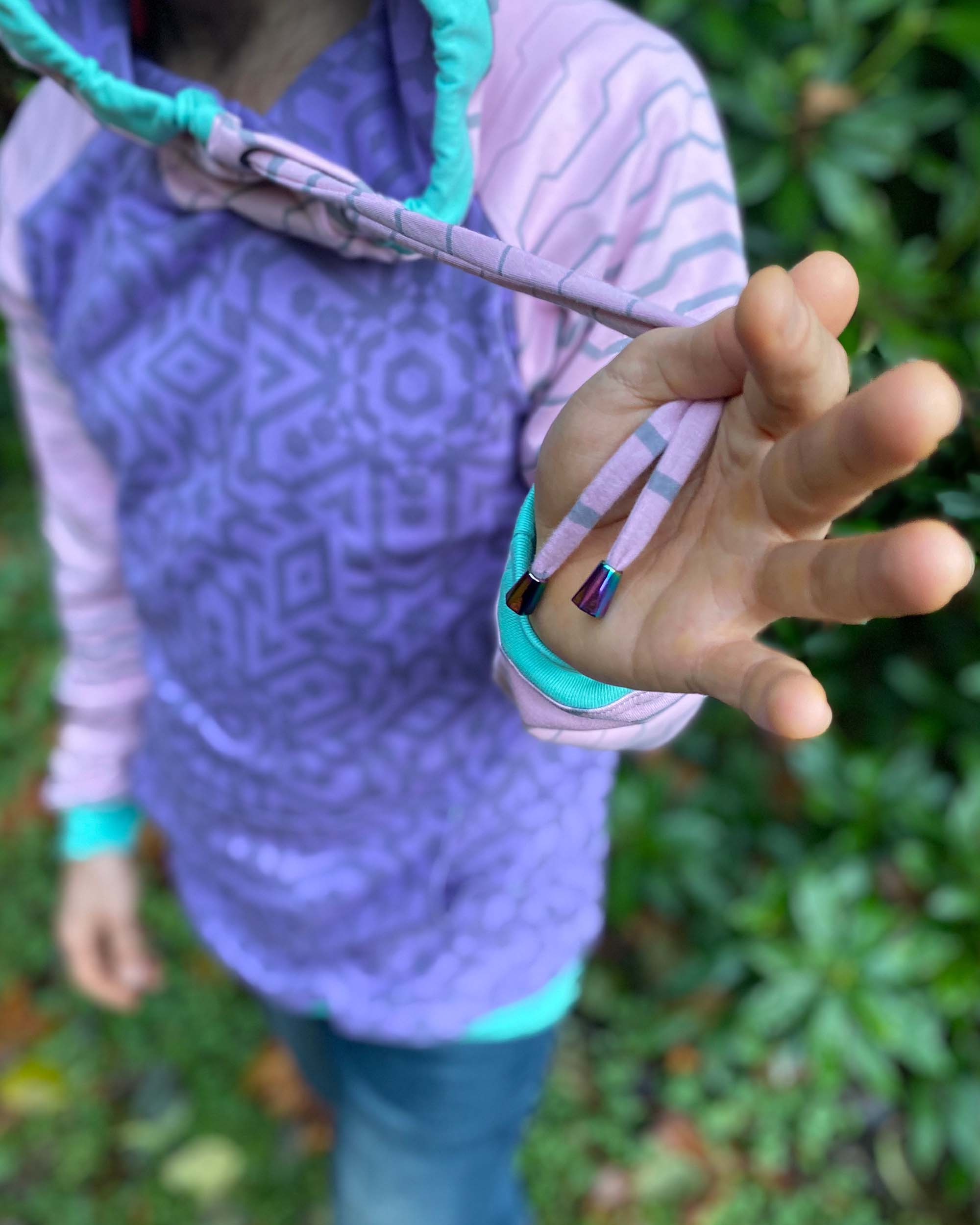 Organic cotton hoodie, lavender and pink fabric with geometric print, detail view of drawcord.