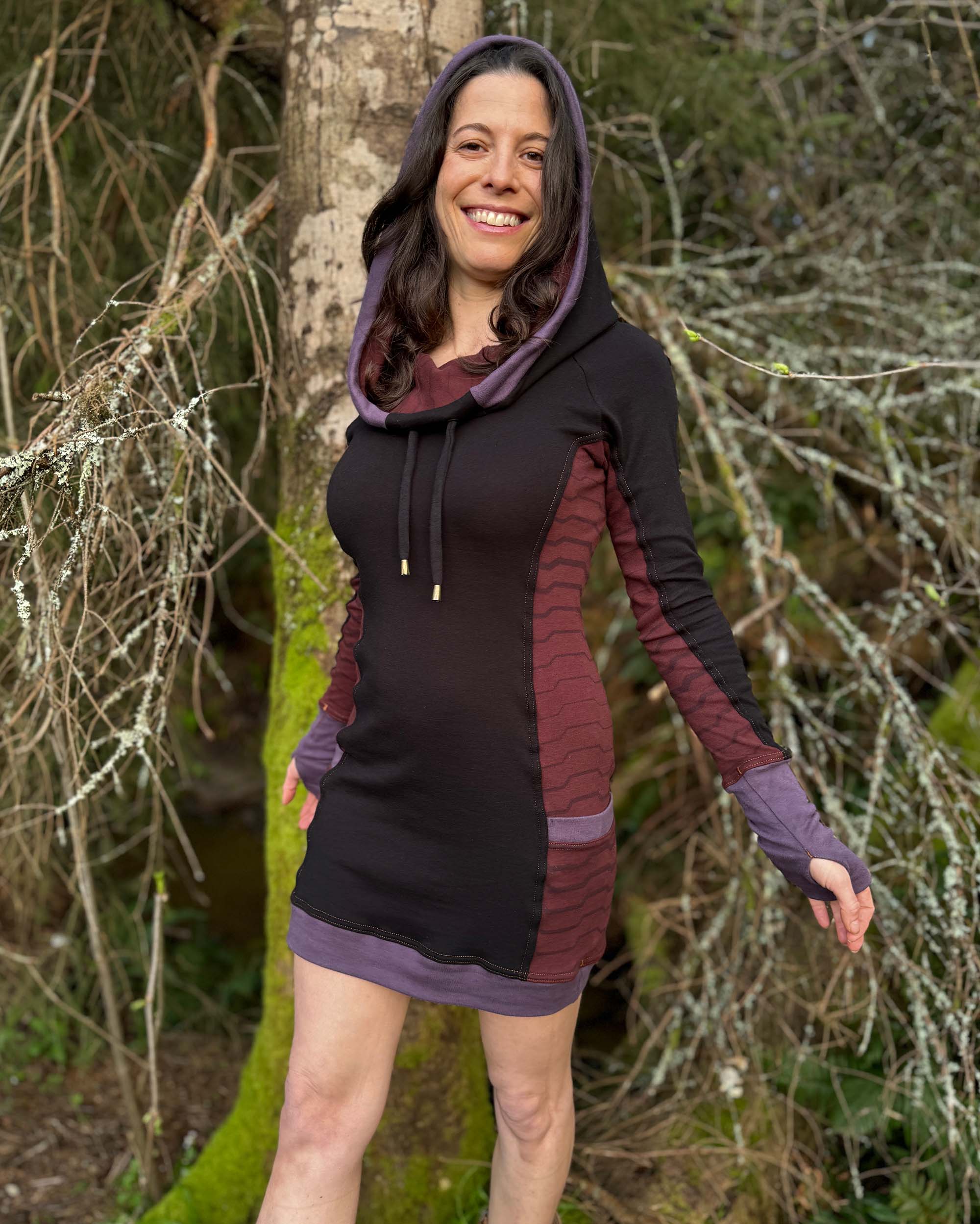 Organic cotton hooded tunic dress, black with geometric brown fabric accents, front view on model in nature.