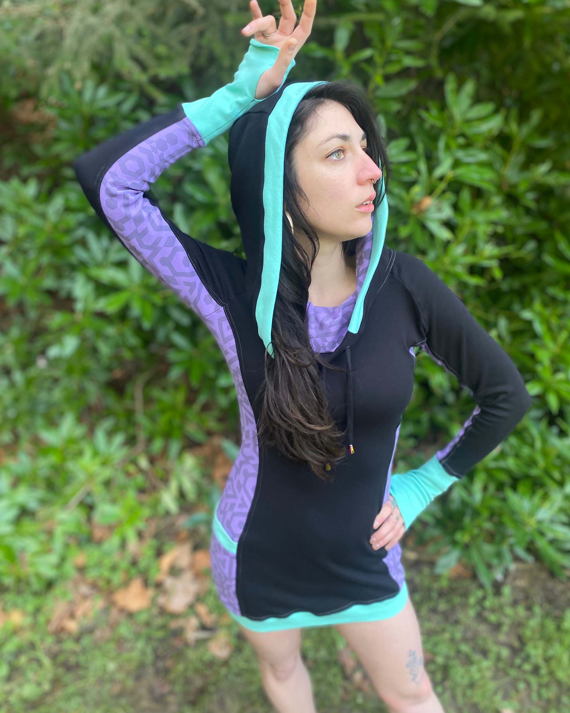 Organic cotton hooded tunic dress, black and lavender fabric with geometric print, front view on model, hood up.