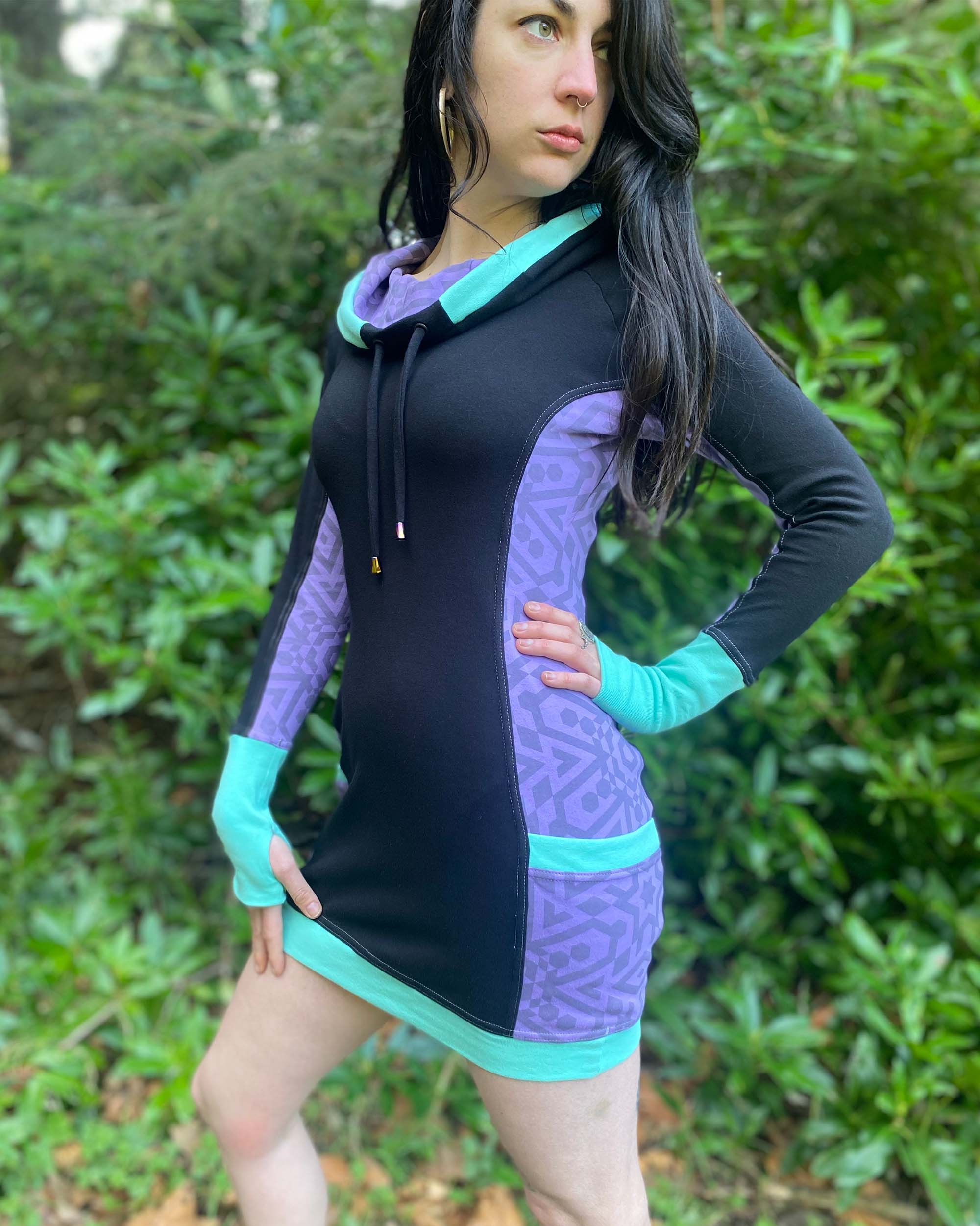 Organic cotton hooded tunic dress, black and lavender fabric with geometric print, front left side view on model.