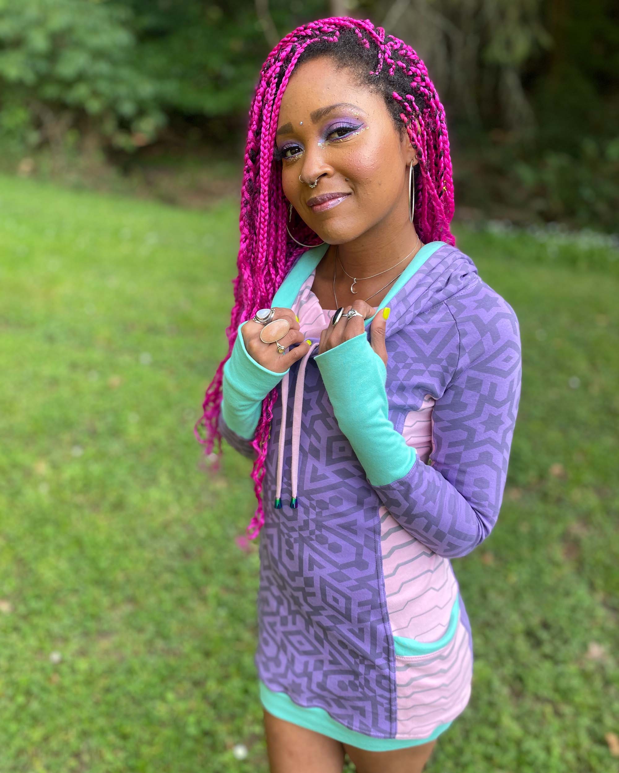 Organic cotton hooded tunic dress, lavender and pink fabric with geometric print, left front side view on model.