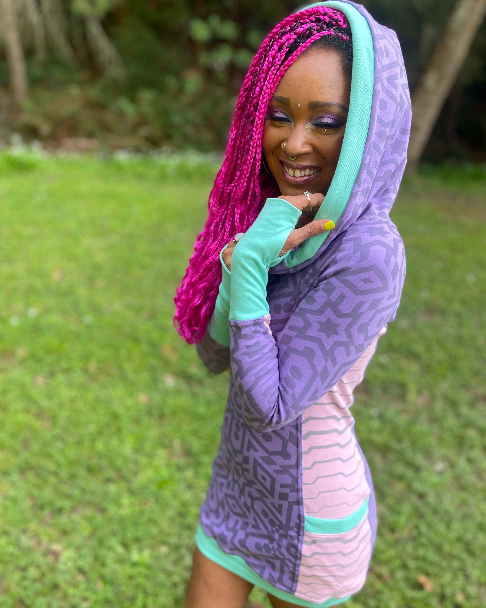 Organic cotton hooded tunic dress, lavender and pink fabric with geometric print, left side view on model, hood up.